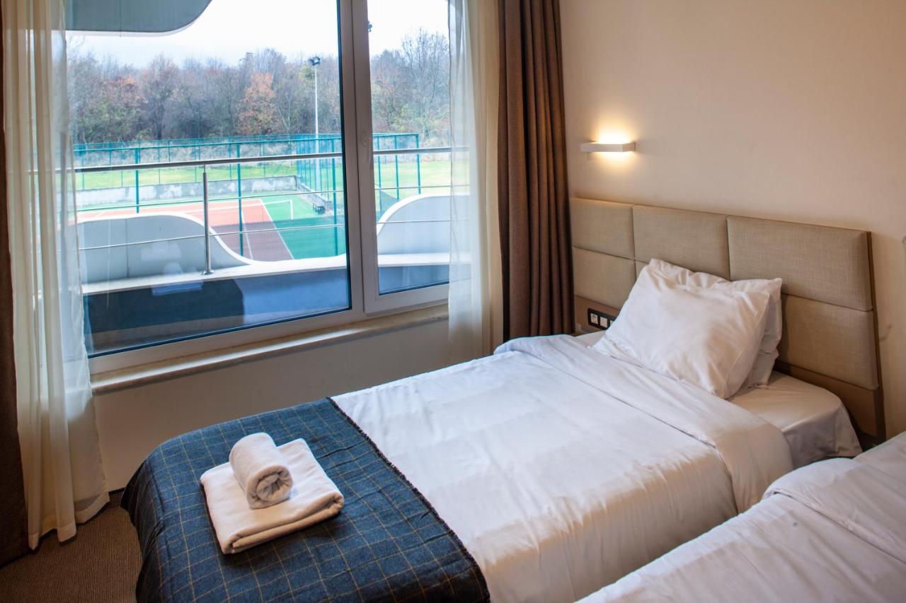 Twin-bed hotel room with balcony view over sports courts, accommodation for athletes at training camp
