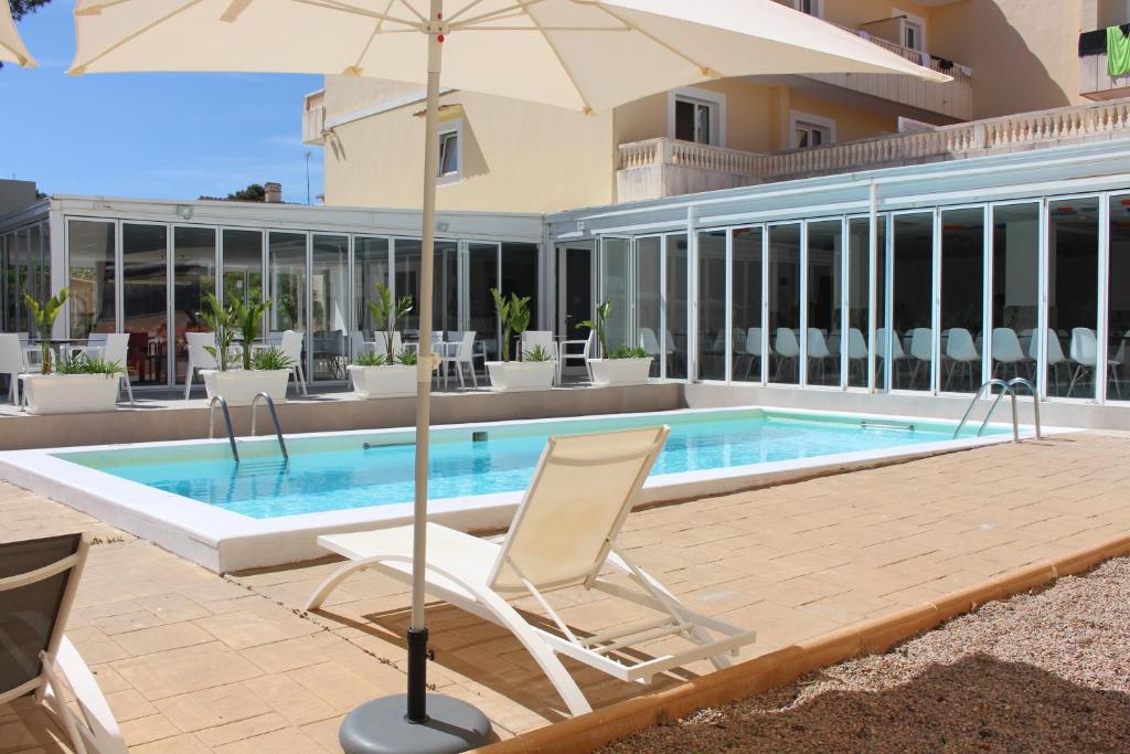 Outdoor pool with sun loungers and parasol beside glass-walled terrace.