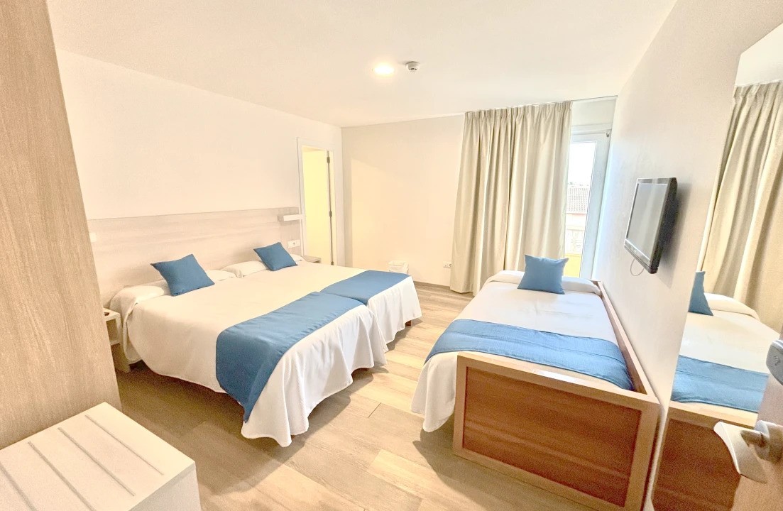 Bright triple room with double and single bed, wall-mounted TV and curtains.