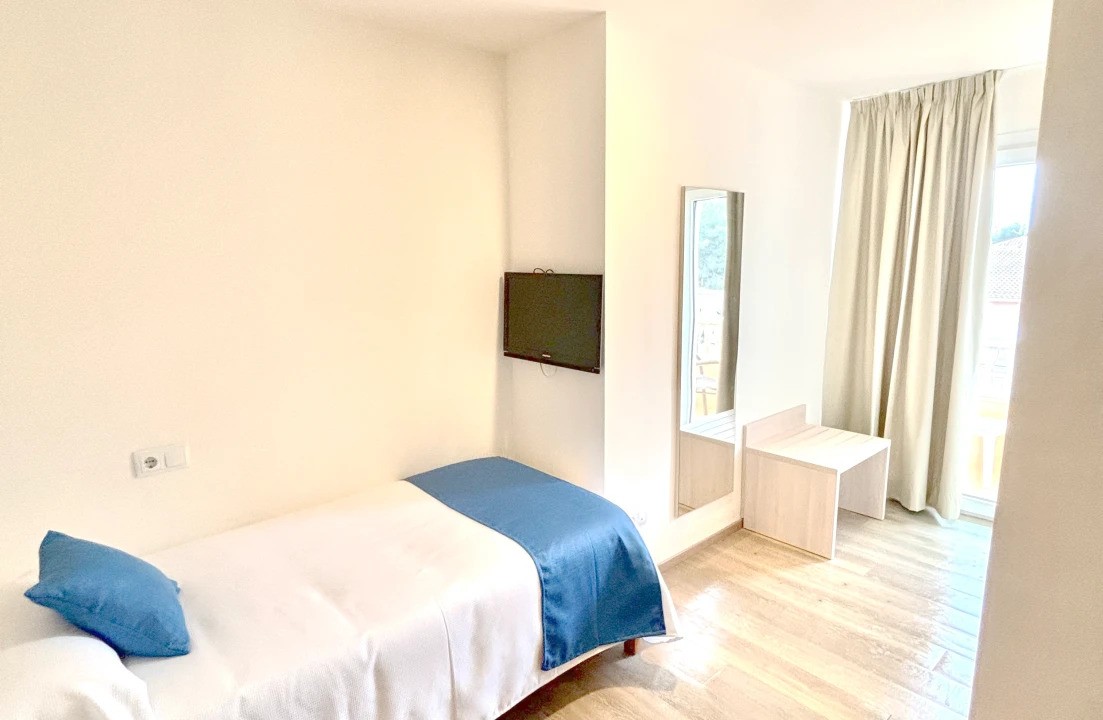 Simple single room with desk, mirror, wall TV and balcony door.