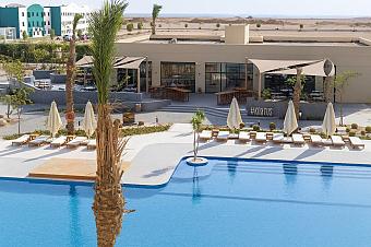 Outdoor pool with sun loungers, umbrellas, and palm trees near resort building
