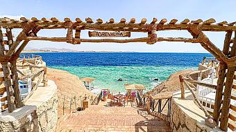 Wooden staircase leading to beach cabanas and turquoise sea under a sign reading “Adrenalina