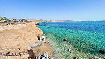 Scenic coastline with crystal-clear water, beach cabanas, and rocky cliffs