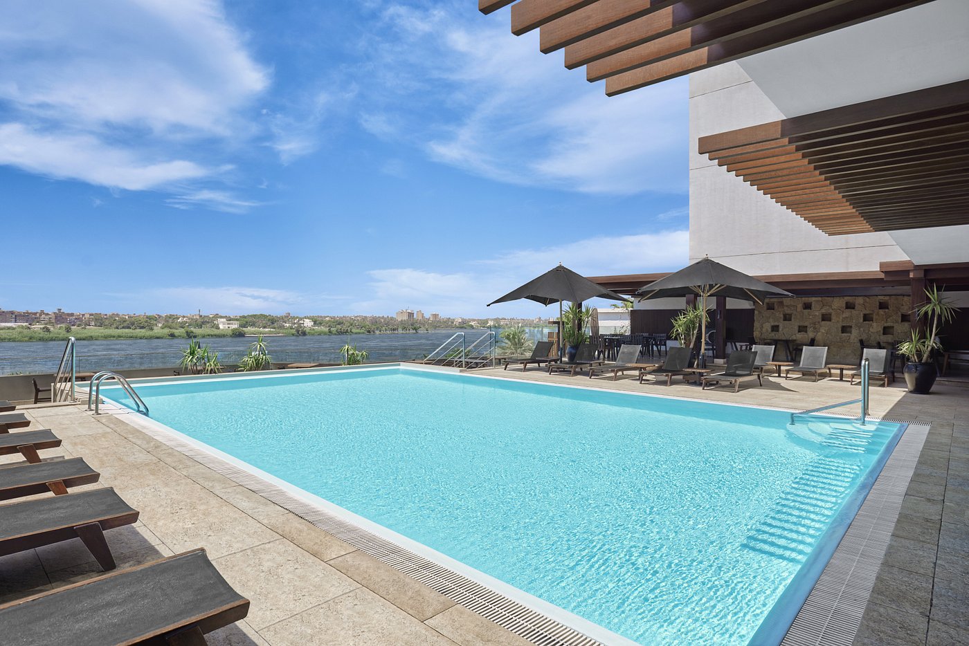 Outdoor pool with loungers and umbrellas overlooking a river—training camp recovery and cooldown area