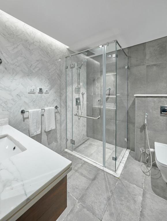 Modern bathroom with glass walk-in shower, gray tile, vanity counter, toilet, and white towels