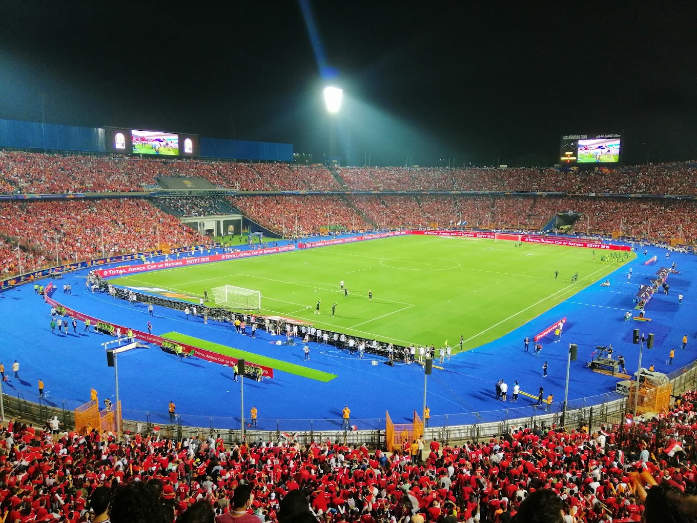 Abendspiel-Atmosphäre in einem voll besetzten Fußballstadion unter Flutlicht, mit blauer Laufbahn ums Feld.