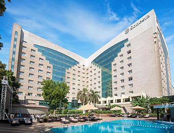 Hotel exterior with outdoor swimming pool, sun loungers, and terrace seating in the courtyard.