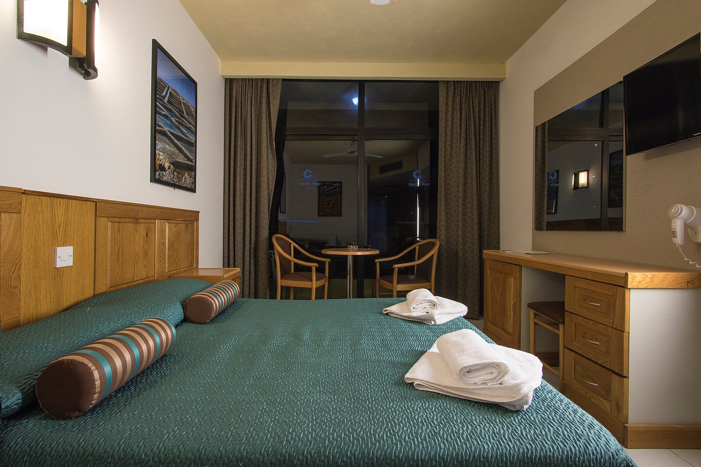 Guest room with double bed, desk, TV, and balcony doors with two chairs.