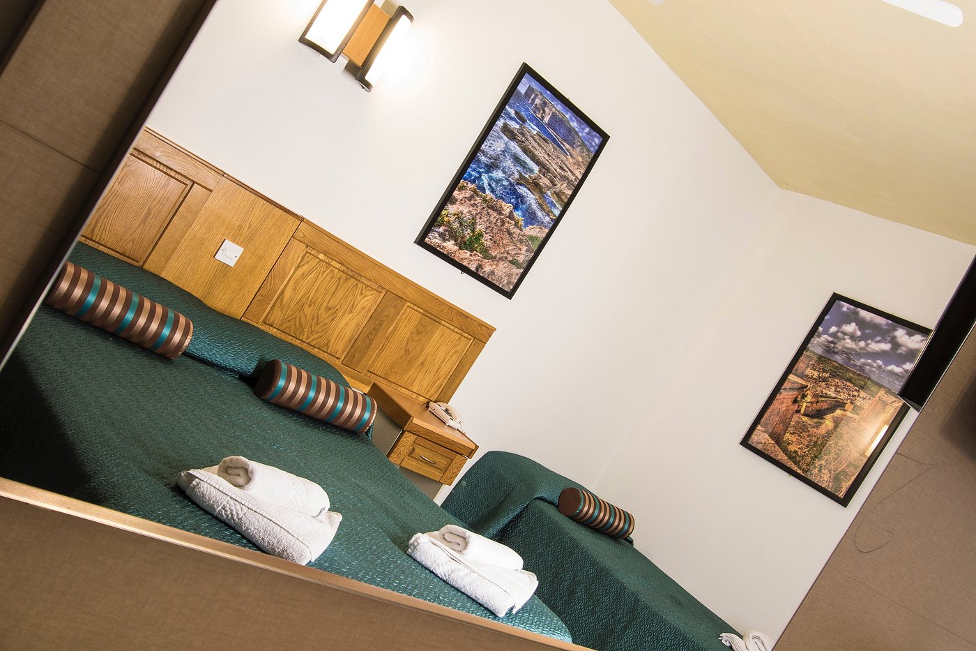 Guest room with twin beds, folded towels, and framed wall art (tilted view).
