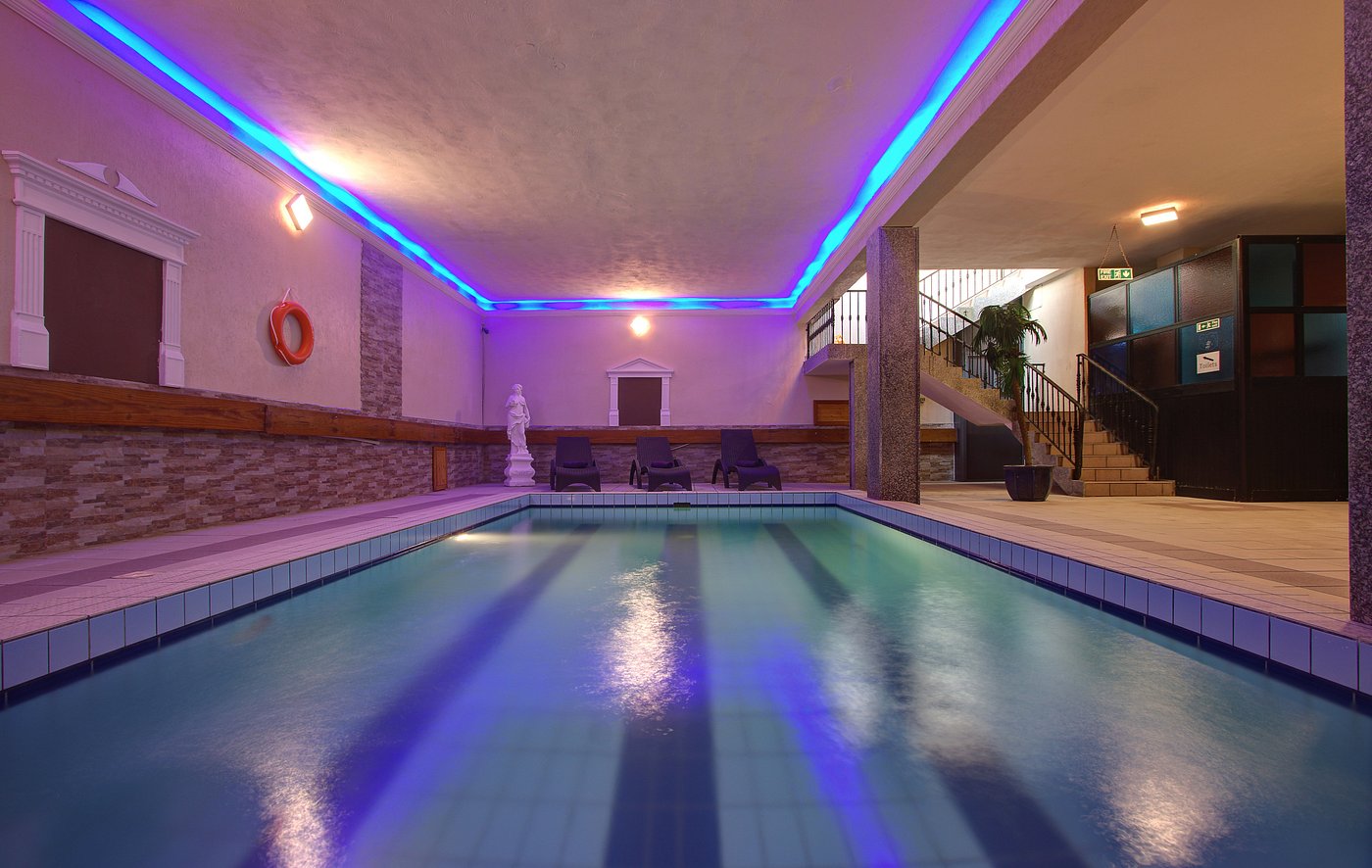 Indoor pool with tiled deck, lounge chairs, and blue ceiling lighting.
