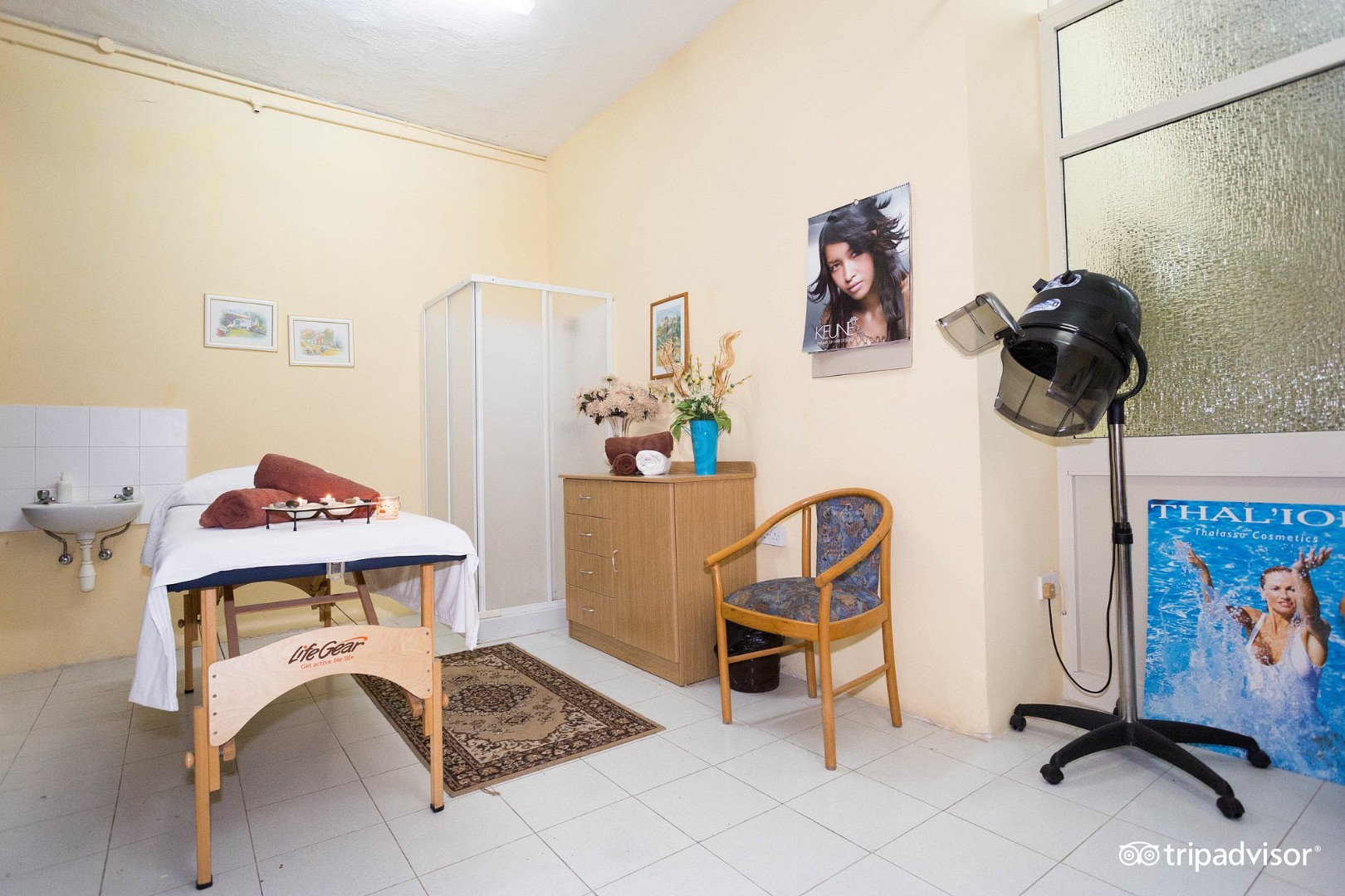 Treatment room with massage table, towels, sink, and salon-style hair dryer.
