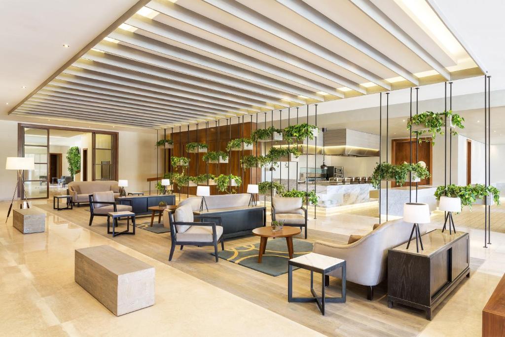 Bright hotel lobby lounge with seating areas, indoor plants, and reception counter.