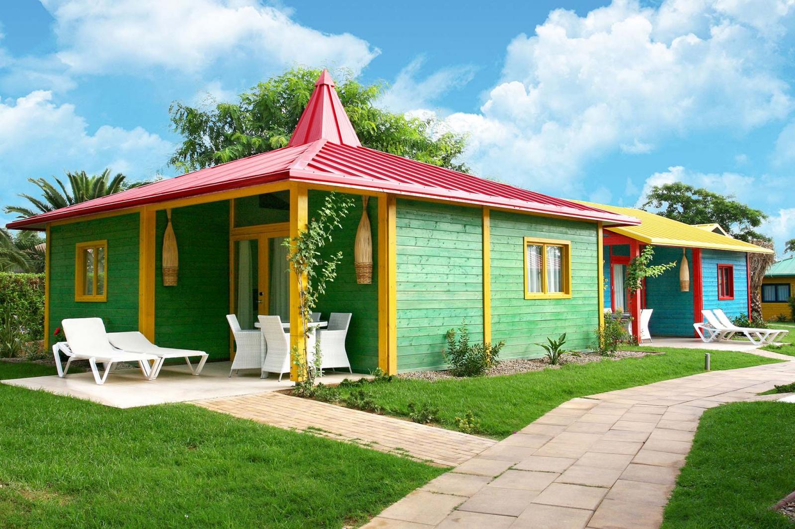 Colorful cottage exterior with patio seating and sun loungers beside a paved path.