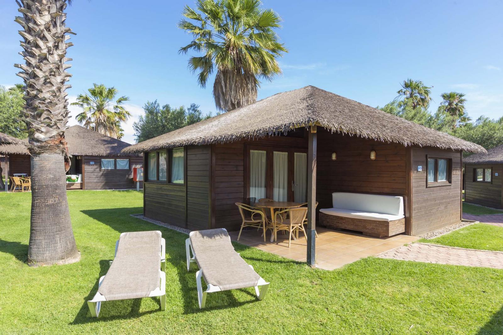 Wooden bungalow with covered patio and sun loungers on a grassy lawn.