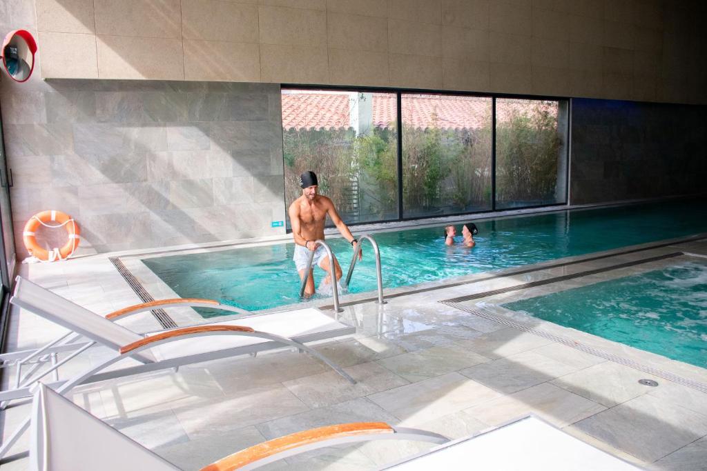 Indoor spa pool with loungers and people in the water.