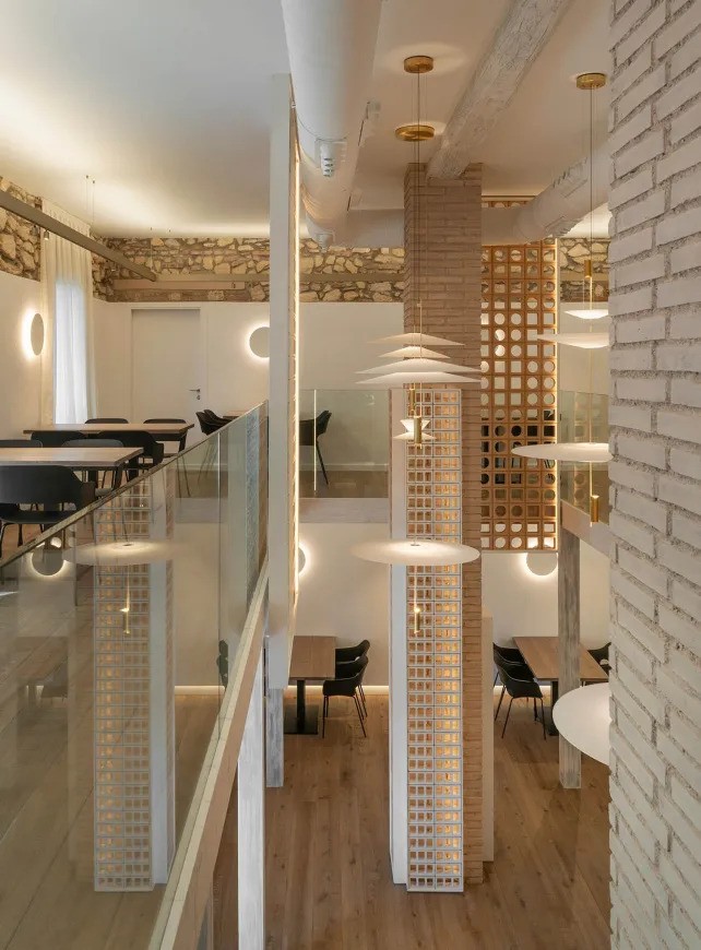 Two-level indoor dining area with tables, glass railing, and modern pendant lights.