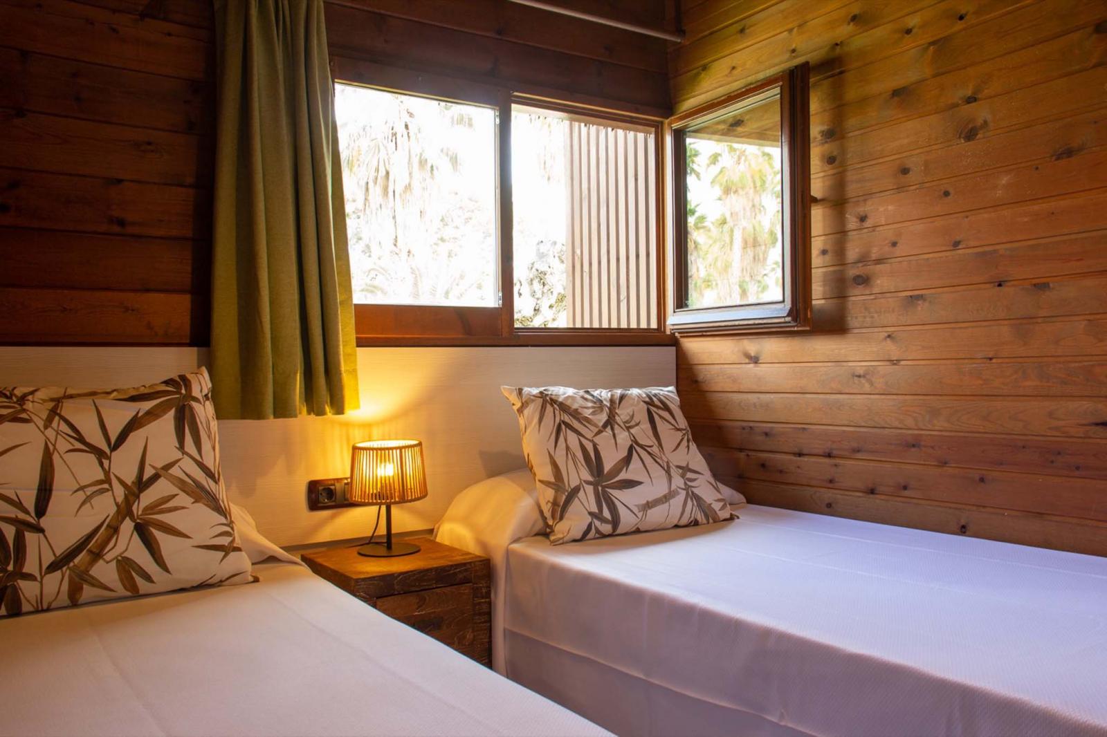 Twin bedroom with wood-paneled walls, bedside lamp, and window.