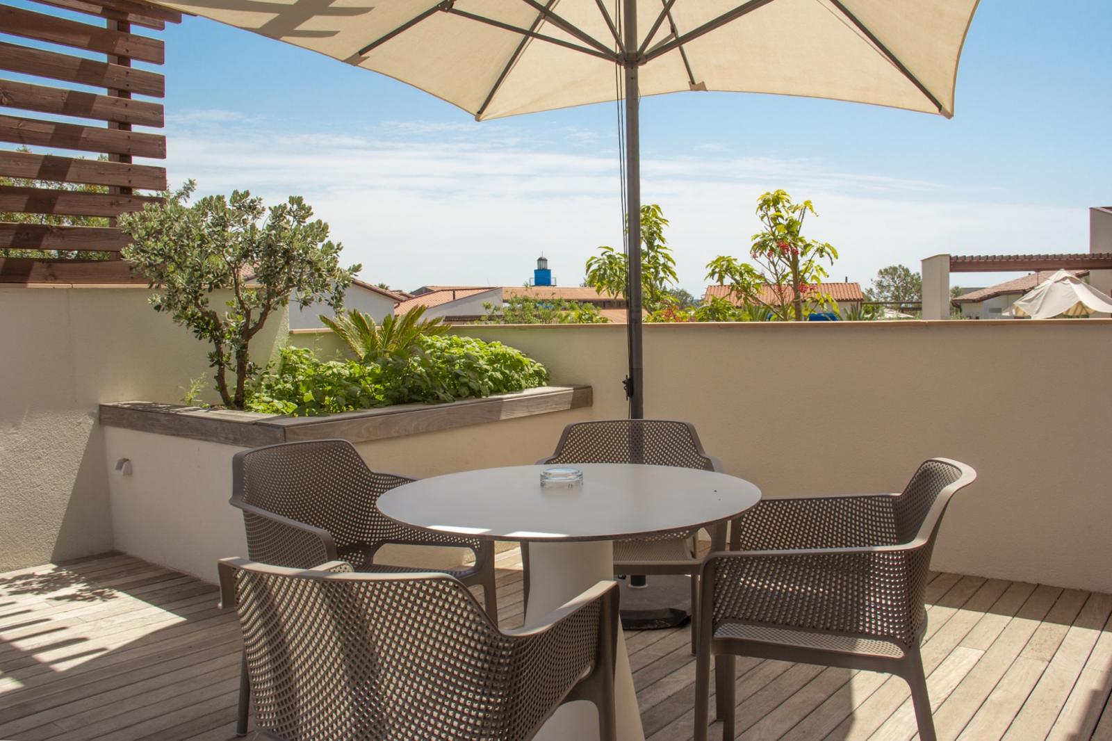 Outdoor terrace with round table, chairs, and large umbrella overlooking rooftops.