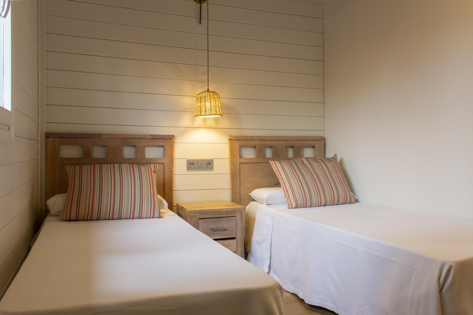 Bright twin room with two single beds, bedside table, and hanging lamp.