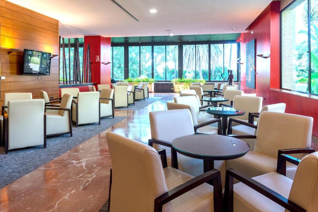 Innenlounge mit Sesseln, kleinen Tischen und großen Fenstern zum Garten.