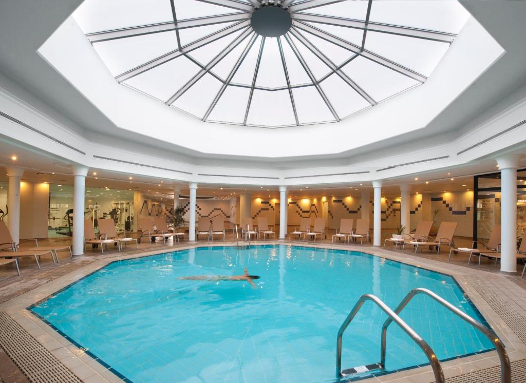 Indoor pool under a skylight with loungers and adjacent fitness area.