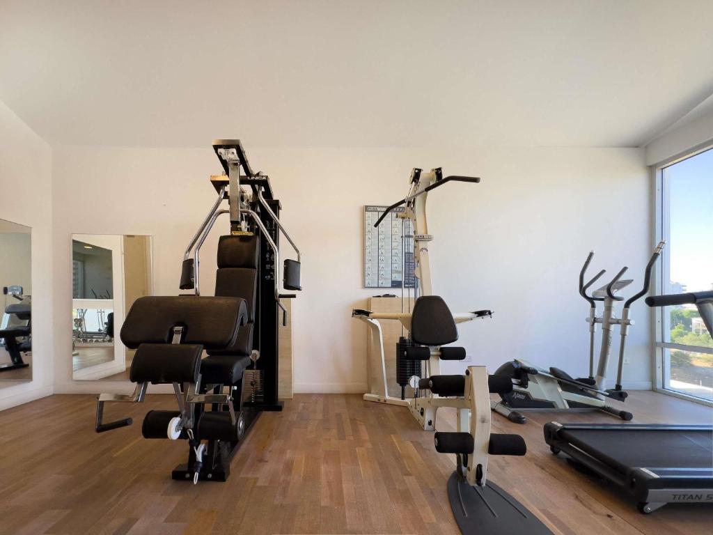 Fitnessraum mit Kraftgeräten, Crosstrainer und Laufband neben großen Fenstern.