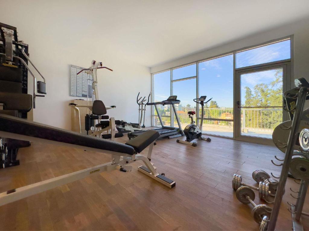 Fitnessraum mit Bank, Laufband, Fahrrad, freien Gewichten und bodentiefen Fenstern.