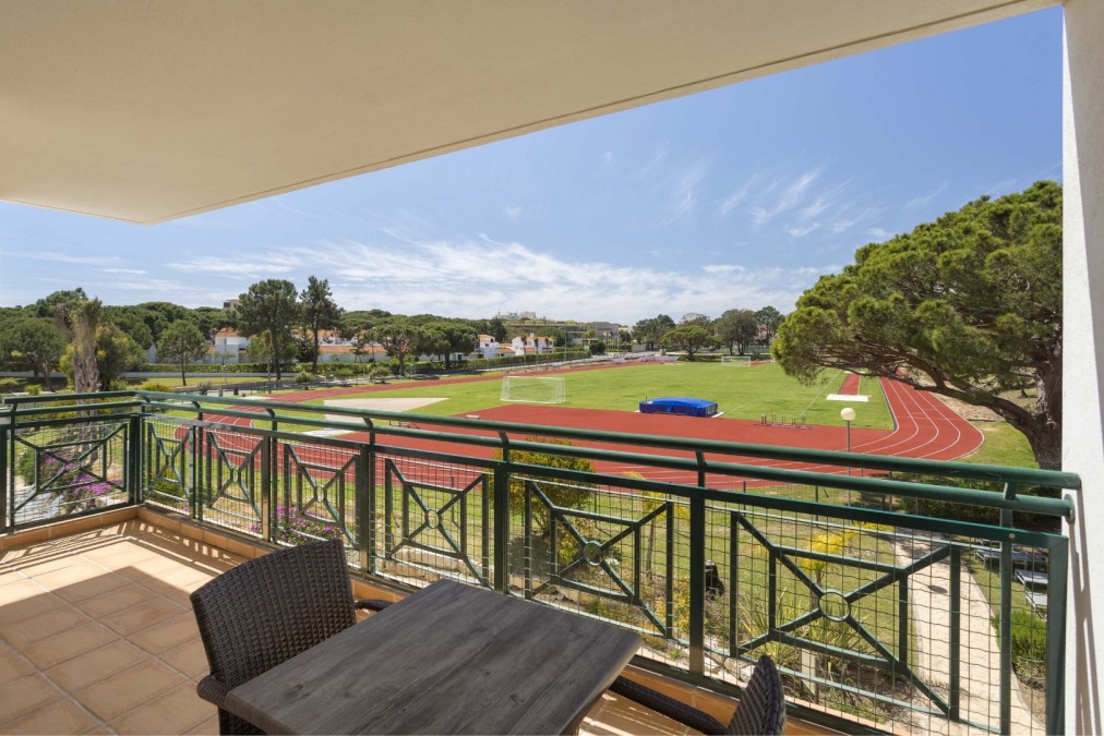 Balkon mit Tisch und Blick auf Laufbahn und Rasenfeld.
