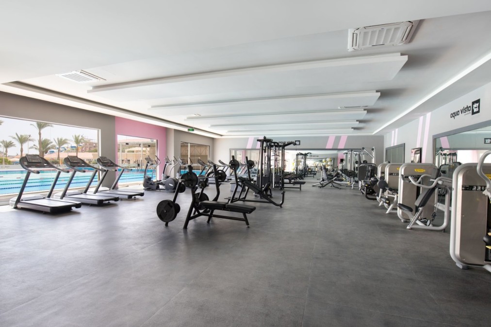 Geräumiges Fitnessstudio mit Laufbändern, Kraftmaschinen und Blick auf den Pool