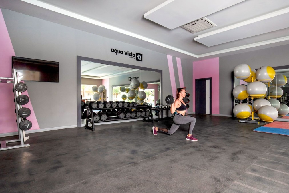 Athlet führt einen Ausfallschritt mit Kurzhanteln im Fitnessstudio mit Gymnastikbällen und Matten aus