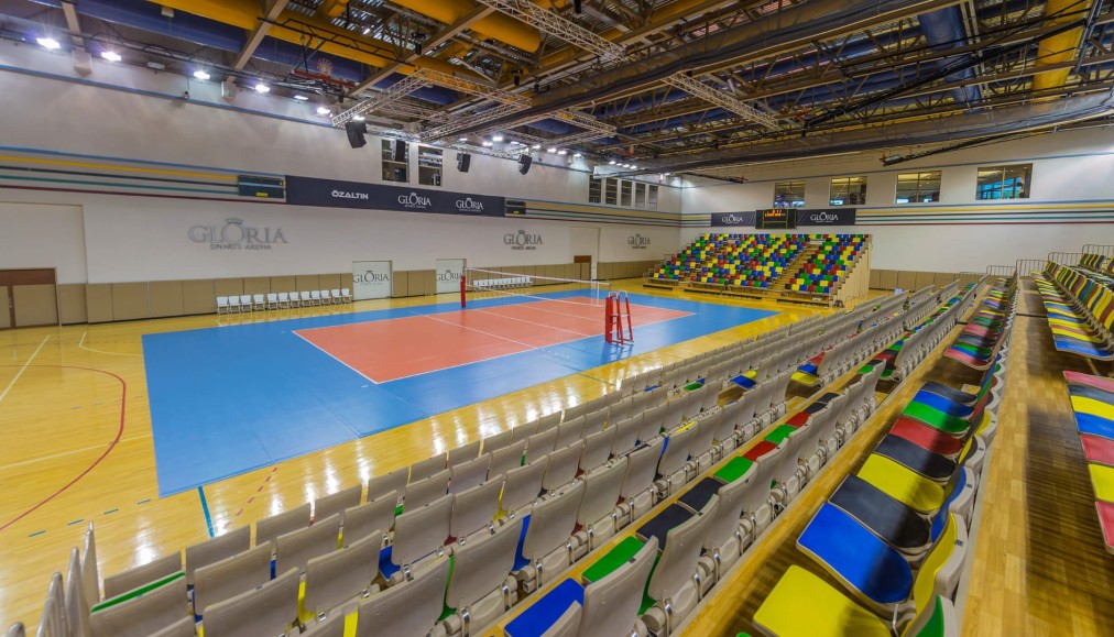 Indoor-Arena für Volleyball mit Netz, Schiedsrichterstuhl und wettkampftauglichem Court-Layout. Tribünen und großzügige Seitenflächen eignen sich für Camps, Spiele und Events.