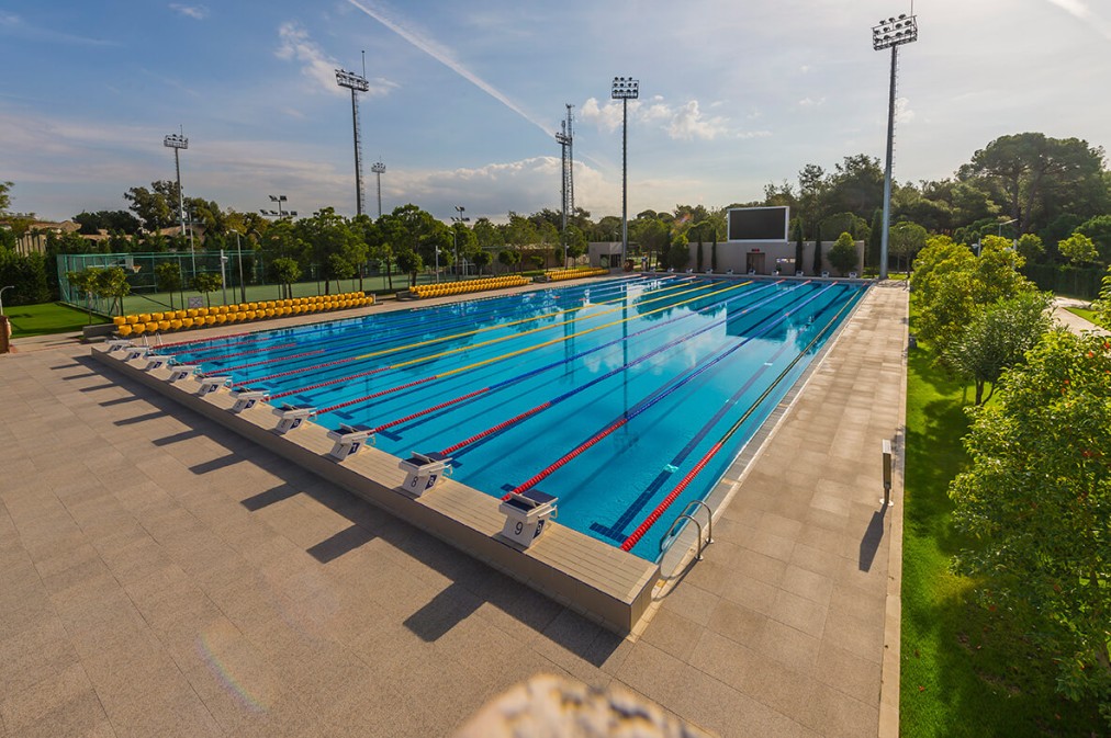 Olympisches Freibad mit Bahnen und Startblöcken für wettkampforientiertes Schwimmtraining. Großzügige Beckenränder und Sitzbereiche eignen sich ideal für Camps und Trainingseinheiten.