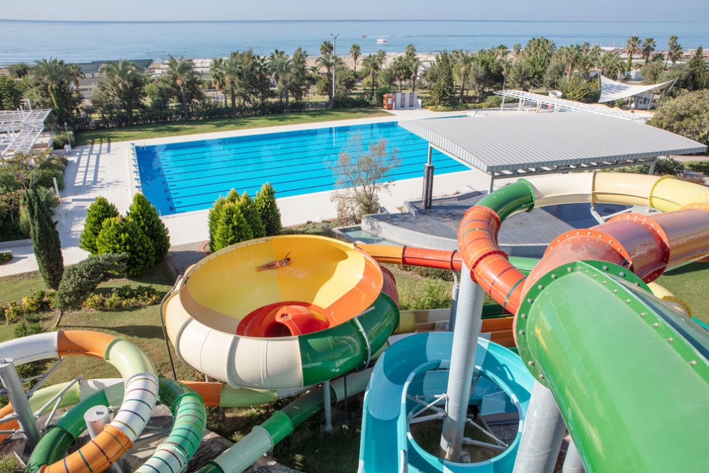 Wasserrutschen mit Blick auf ein großes olympisches Schwimmbecken und Meerblick im Hintergrund.