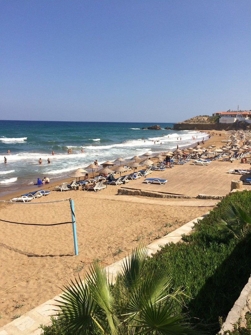 Sandstrand mit Sonnenliegen, Sonnenschirmen und Volleyballnetz am Meer