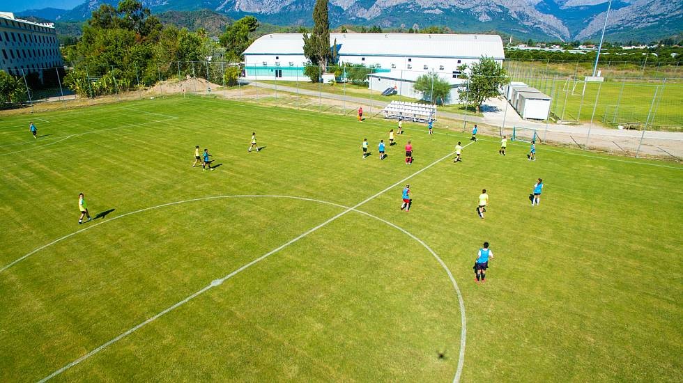 Fußball-Trainingseinheit auf einem Rasenplatz mit Bergkulisse hinter der Anlage.