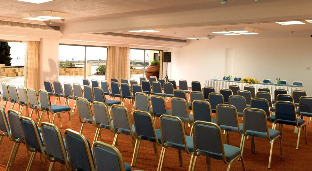Präsentationssaal mit Reihen blauer Stühle und einem vorderen Tisch für Teamseminare oder Workshops