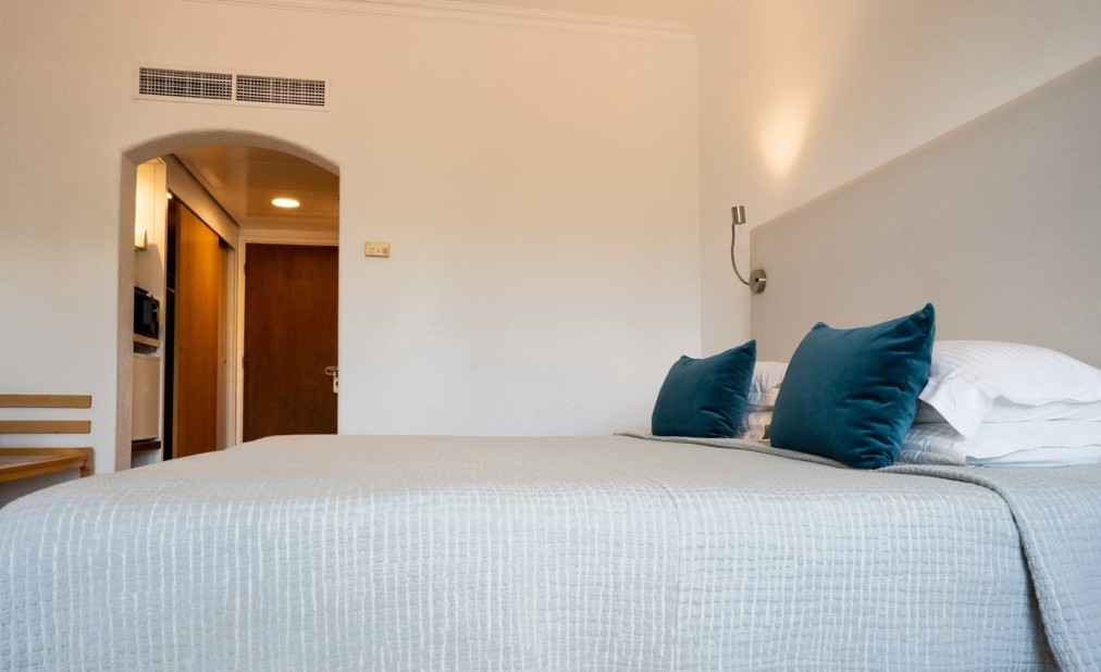 Hotelzimmer mit großem Bett, grauer Bettwäsche und türkisfarbenen Kissen in minimalistischem Design