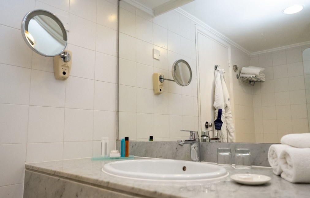 Modernes Badezimmer mit weißen Fliesen, Waschbecken, Spiegel und Bademantel an der Wand