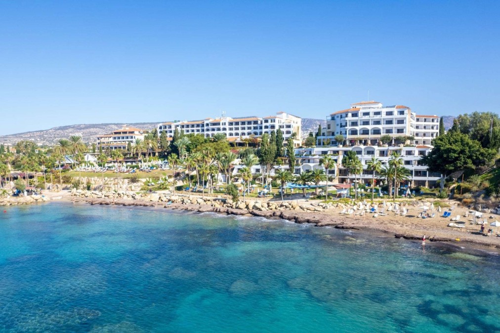 Hotelkomplex am Meer mit weißen Gebäuden und Palmen mit Blick auf eine klare blaue Küste