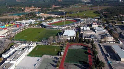 Hohe Luftaufnahme des Sportkomplexes Rio Maior mit Stadion, Plätzen, Trainingsbereichen und umliegender Landschaft.