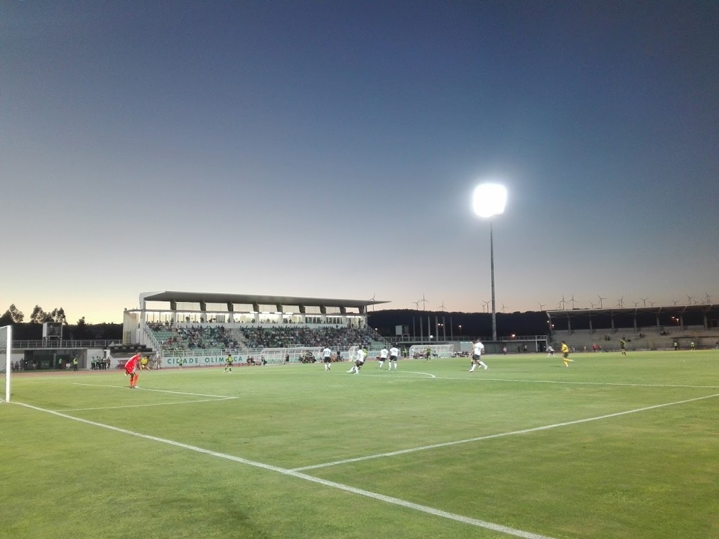 Flutlicht-Fußballstadion in der Dämmerung mit spielenden Teams auf dem Spielfeld.