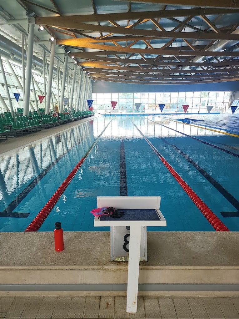 Hallen-Schwimmbecken mit Startblock, Leinen und Sitzreihen entlang des Beckenrands.