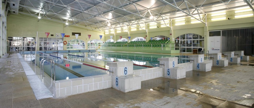 Hallenbad mit Startblöcken, Schwimmleinen und Zuschauertribüne für Training und Wettkämpfe.