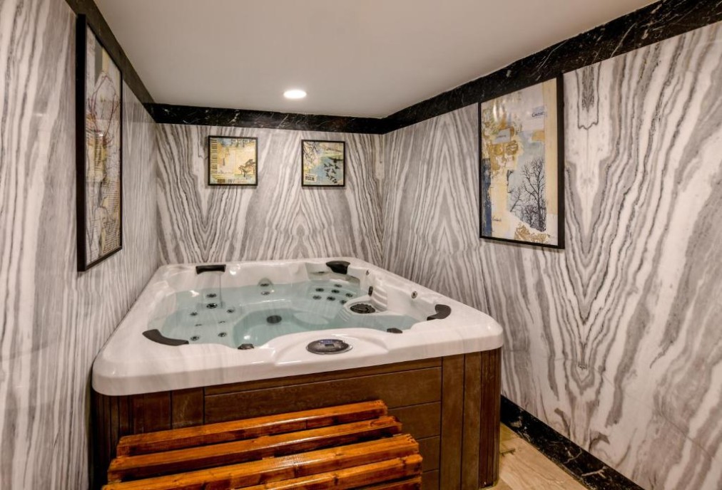 Whirlpool in einem Spa-Raum mit gemusterten grauen Marmorwänden, Holzbank und gerahmter Wandkunst