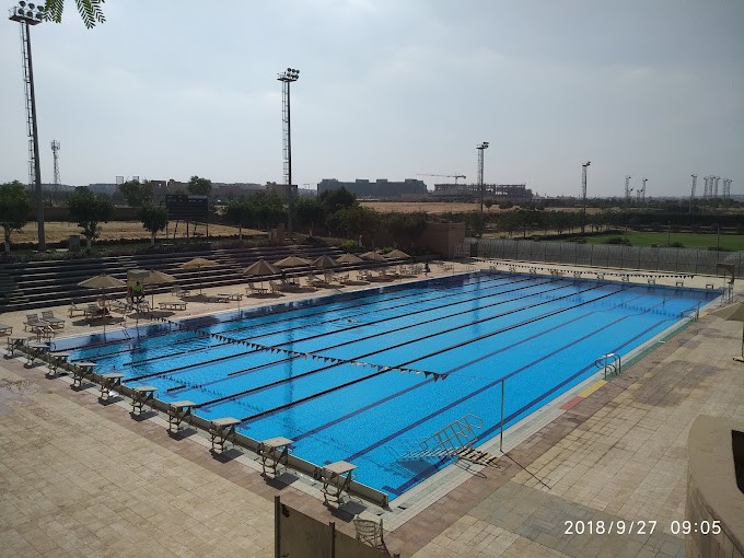 Wettkampf-Freibad mit Bahnleinen und Startblöcken, umgeben von Sitzreihen und Sonnenschirmen.
