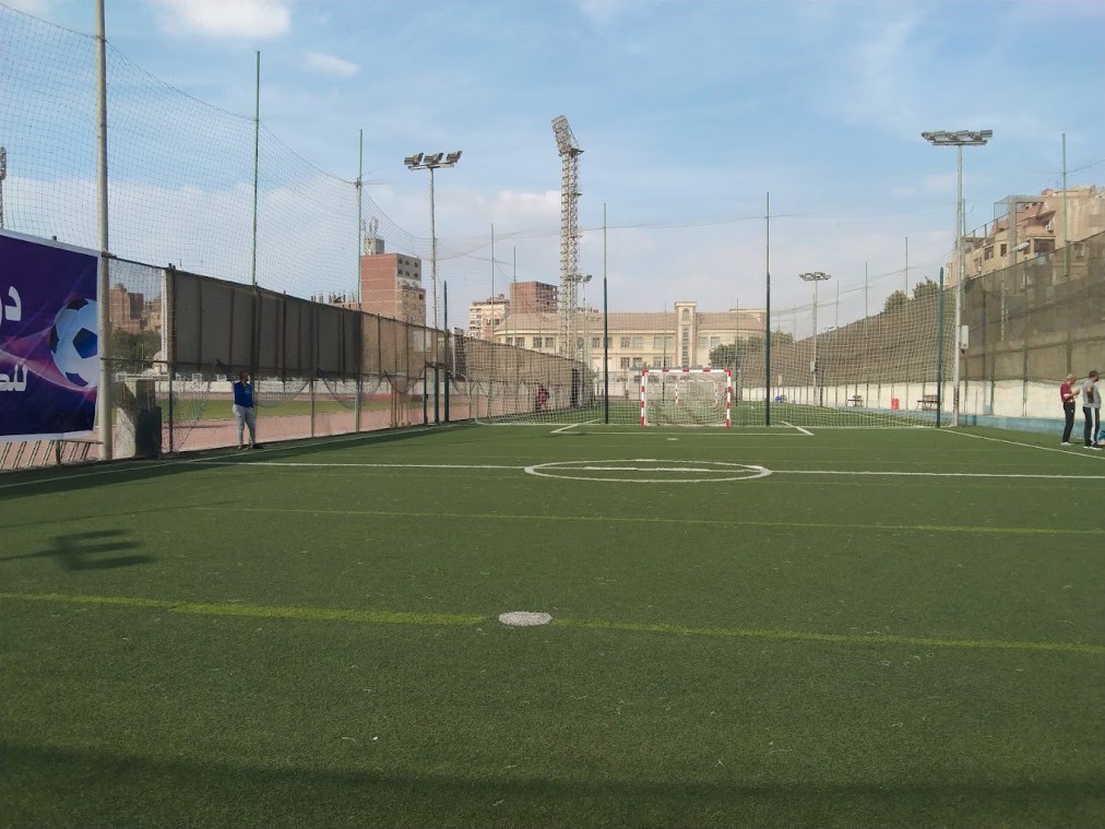 Eingezäunter Kunstrasen-Mini-Fußballplatz mit Tor und Flutlichtmasten.