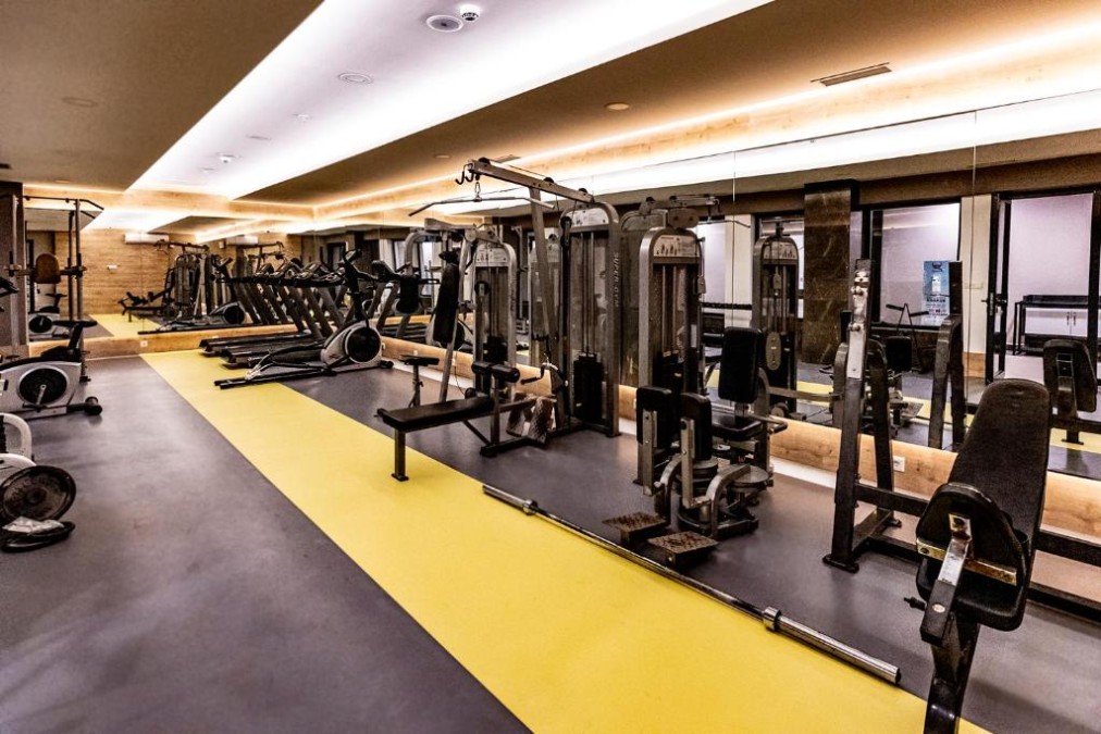 Innen-Fitnessraum mit Laufbändern, Kraftgeräten, Bänken und Spiegelwand für Workouts.
