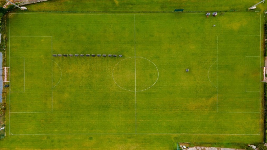 Luftaufnahme eines Rasen-Fußballplatzes in voller Größe mit Toren und Mittelkreis.