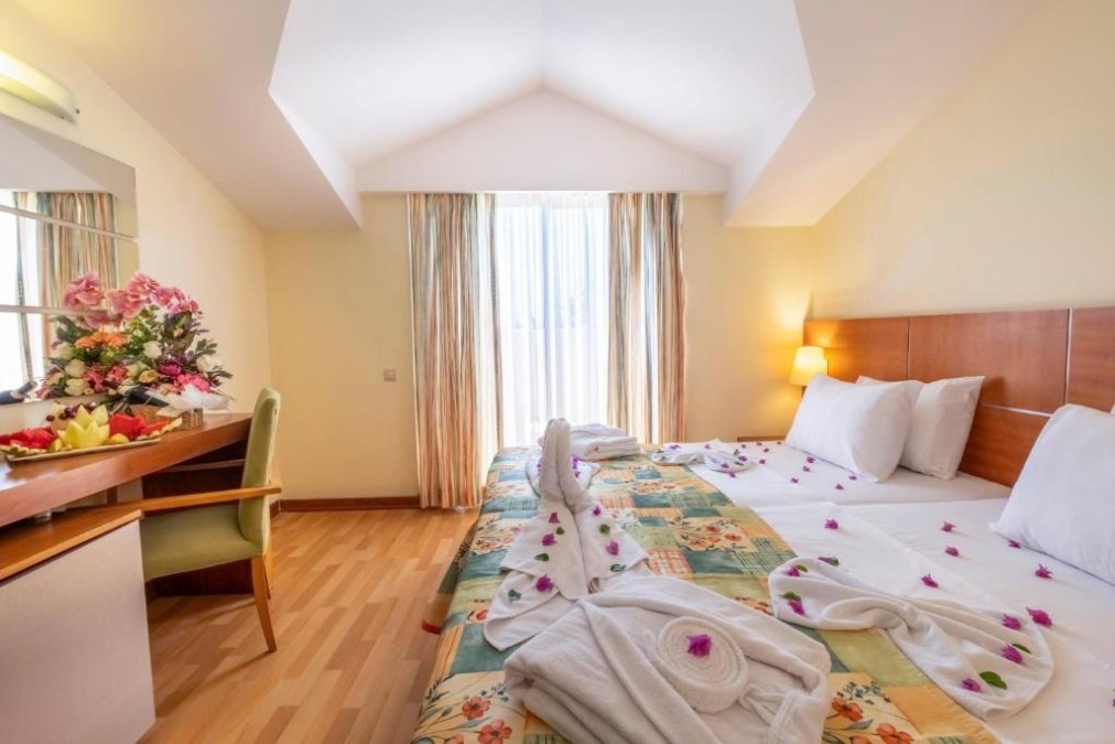 Loftartiges Hotelzimmer mit Doppelbett, Schreibtisch und hohem Fenster mit Vorhängen.