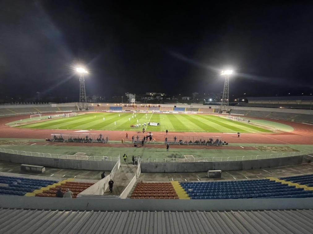 Nachtaufnahme eines Fußballspiels in einem beleuchteten Stadion mit umlaufender Laufbahn.